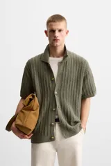 Camisa verde militar de punto con estructura abierta, corte regular fit, cuello solapa, manga corta y cierre frontal con botones.