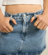 Minifalda de denim azul claro con cintura media, trabillas, bolsillos y cierre frontal con botón y cremallera.