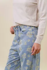 Pantalón de jean de tiro medio-alto, pierna ancha y lavado celeste claro, con estampado floral en tono amarillo pálido.