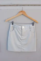 Minifalda de cuero ovino color blanco hueso o hielo, con diseño de cinco bolsillos (dos delanteros, dos traseros y un ticket pocket) y cierre frontal con botón blanco.