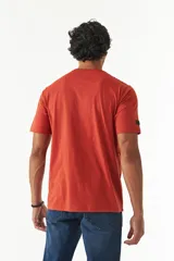 Remera de manga corta color ladrillo, con cuello redondo y estampado con texto y diseño abstracto en el frente.