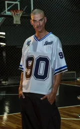 Camiseta estilo jersey de fútbol americano, color blanco, con cuello en V ribeteado en azul. Presenta el número "90" grande en el frente en azul marino con borde blanco. Tiene bordados en el pecho como "Lx." y "Ravers", y números pequeños en las mangas. Los puños tienen franjas azules y negras.