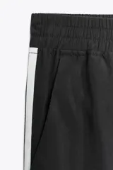 Pantalón negro de tiro alto con cintura elástica, bolsillos delanteros y detalle de banda lateral blanca.