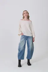 Sweater holgado de tejido ligero, color beige claro, con escote asimétrico que deja un hombro al descubierto.