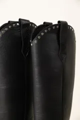 Bota texana alta de cuero negro con puntera fina y tachas plateadas en el borde superior.