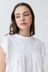 Blusa blanca de algodón con cuello redondo fruncido y mangas cortas con volados.