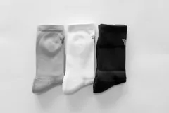 Pack de tres pares de medias de caña alta, una blanca, una gris y una negra, con logo en el tobillo.