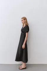 Vestido midi negro satinado con escote pico, pliegues en el busto y mangas cortas. Cintura entallada y cierre lateral con cremallera oculta.