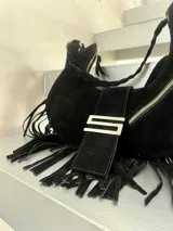 Cartera negra tipo hobo de gamuza con flecos, cierre superior con cremallera y asa de hombro trenzada.