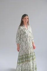 Vestido largo color blanco con estampado geométrico en verde y ocre. Tiene cuello mao, mangas largas abullonadas y corte imperio con falda escalonada.