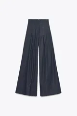 Pantalón de jean azul oscuro, de tiro muy alto y pierna ancha. Presenta pinzas en la parte delantera y cierre trasero con cremallera oculta.