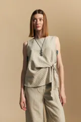 Top sin mangas color beige con finas rayas verticales negras. Presenta un diseño con lazada ajustable en el lateral de la cintura.