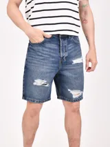 Bermuda de jean azul con efecto lavado y rotos. Diseño clásico de cinco bolsillos, cierre con botón y cremallera.