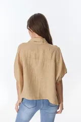 Camisa color beige de lino con cuello camisero, manga corta y cierre frontal con botones. Presenta detalles de encaje en el cuello, el frente y las mangas.