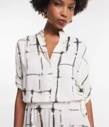 Vestido midi de viscosa color blanco con estampado de bloques negros, corte evasé, mangas cortas, cuello camisero, lazo en la cintura y cierre frontal con botones.