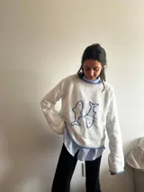 Sweater blanco de punto con cuello redondo y diseño de dos peces azules bordados en el frente.