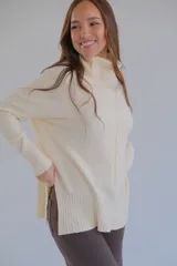Sweater color crema de corte recto con cuello alto y aberturas laterales.