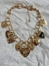 Collar dorado con doble cadena, una de eslabones grandes y otra de eslabones pequeños, con múltiples dijes de corazones dorados y negros.