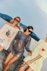 Sweater tejido color crema con cuello amplio que deja un hombro al descubierto. Presenta un estampado con dibujos de estilo boceto en negro y rojo, y detalles de roturas en las mangas.