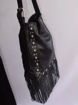 Bolso tipo bandolera de cuero negro con flecos y tachas plateadas. Tiene correa regulable, forro interior y bolsillo interno.