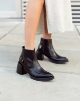 Botín corto de cuero negro, estilo cowboy moderno, con textura de cocodrilo en la caña y puntera cuadrada. Posee un tacón ancho y geométrico, y cierre lateral.