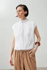 Blusa blanca sin mangas con cuello alto y detalles de puntilla.