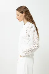 Campera blanca de broderie con cierre frontal, cuello redondo y mangas largas.