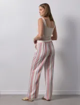 Pantalón de lino color blanco con rayas verticales rosas y celestes. Tiene pretina ancha elastizada con lazo de ajuste y bolsillos inclinados en la parte delantera.