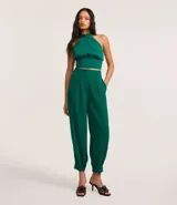 Pantalón zanahoria de tejido plano color verde esmeralda, con trabillas en la cintura, cierre tradicional, pliegues en la frente y pinzas en la parte trasera.