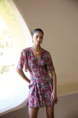 Vestido corto con estampado floral en tonos rojo y gris, escote en V, mangas cortas con volados, frunces en delantero y espalda, y bolsillos delanteros.