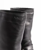 Bota de cuero color marrón oscuro, de caña media, con hebilla y tachas decorativas.