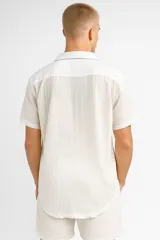 Camisa de lino color crudo, de manga corta, con cuello camisero y bolsillo de parche en el pecho.