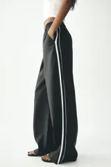 Pantalón negro de tiro alto con cintura elástica, bolsillos delanteros y detalle de banda lateral blanca.