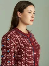 Cardigan de punto color borgoña con diseño geométrico en blanco y detalles en azul. Tiene cuello redondo, cierre frontal con botones rojos y mangas largas con puños acanalados.