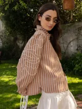 Camisa a rayas verticales color marrón y blanco, con cuello con volados, mangas largas abullonadas con bordado y puños elásticos.