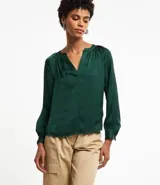 Blusa verde esmeralda de tela satinada, con escote en V, mangas largas con puños abotonados y espalda fruncida.