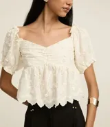 Blusa peplum color blanco, confeccionada en algodón, con escote corazón, mangas abullonadas cortas y bordado floral.