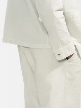 Pantalón de vestir color crema, confeccionado en tejido ligero de algodón con textura seersucker. Tiene corte recto, bolsillos laterales y traseros, cierre con botón y cremallera, y parche con logo de la marca.