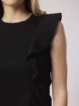 Musculosa negra de algodón con elastano, corte recto y cuello redondo. Presenta volados en las sisas con tejido plumetí (con puntos en relieve).