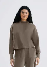 Buzo color beige en tela acanalada con cuello alto y puños ajustados.