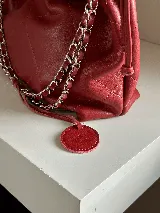 Cartera tipo bolso capitoneada de cuero color rojo, con asa de cadena plateada entrelazada con cuero. Forrada por dentro y con bolsillo interno.