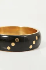 Pulsera rígida negra con puntos dorados.
