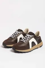 Zapatillas deportivas marrones con detalles en blanco y suela color caramelo.