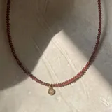 Gargantilla de cuentas facetadas color borgoña con dije circular dorado con piedra transparente.