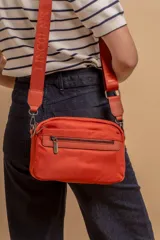 Bandolera color rosa viejo con detalles en cuero marrón claro, múltiples cremalleras metálicas y herrajes plateados. Incluye correa ancha ajustable con el logo de la marca.