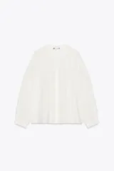 Camisa blanca de ramio con cuello redondo, mangas largas con puños elásticos y cierre frontal con botones.