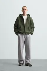 Sudadera negra con capucha ajustable, corte relaxed fit, confeccionada en tejido de algodón compacto con interior en rizo. Cuenta con manga larga, bolsillos frontales tipo canguro, acabados en rib y cierre frontal con cremallera.