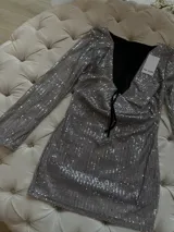Vestido corto plateado de lentejuelas con mangas largas acampanadas y espalda descubierta que se ata con tiras.