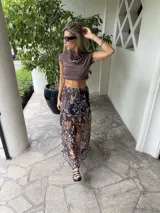 Falda larga de tela estampada con flores y hojas en tonos marrones, negros y violetas. Tiene elástico en la cintura.