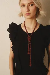 Remera negra sin mangas con volados en los hombros y escote en V. Incluye un collar largo de cuentas con un nudo decorativo. Jeans de tiro bajo.